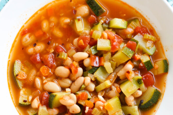 A white bowl full of White Bean and Zucchini Soup.